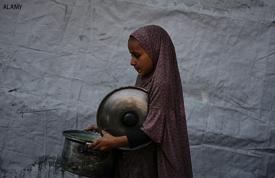 A Palestinian child carries a pot of donated food from a community kitchen